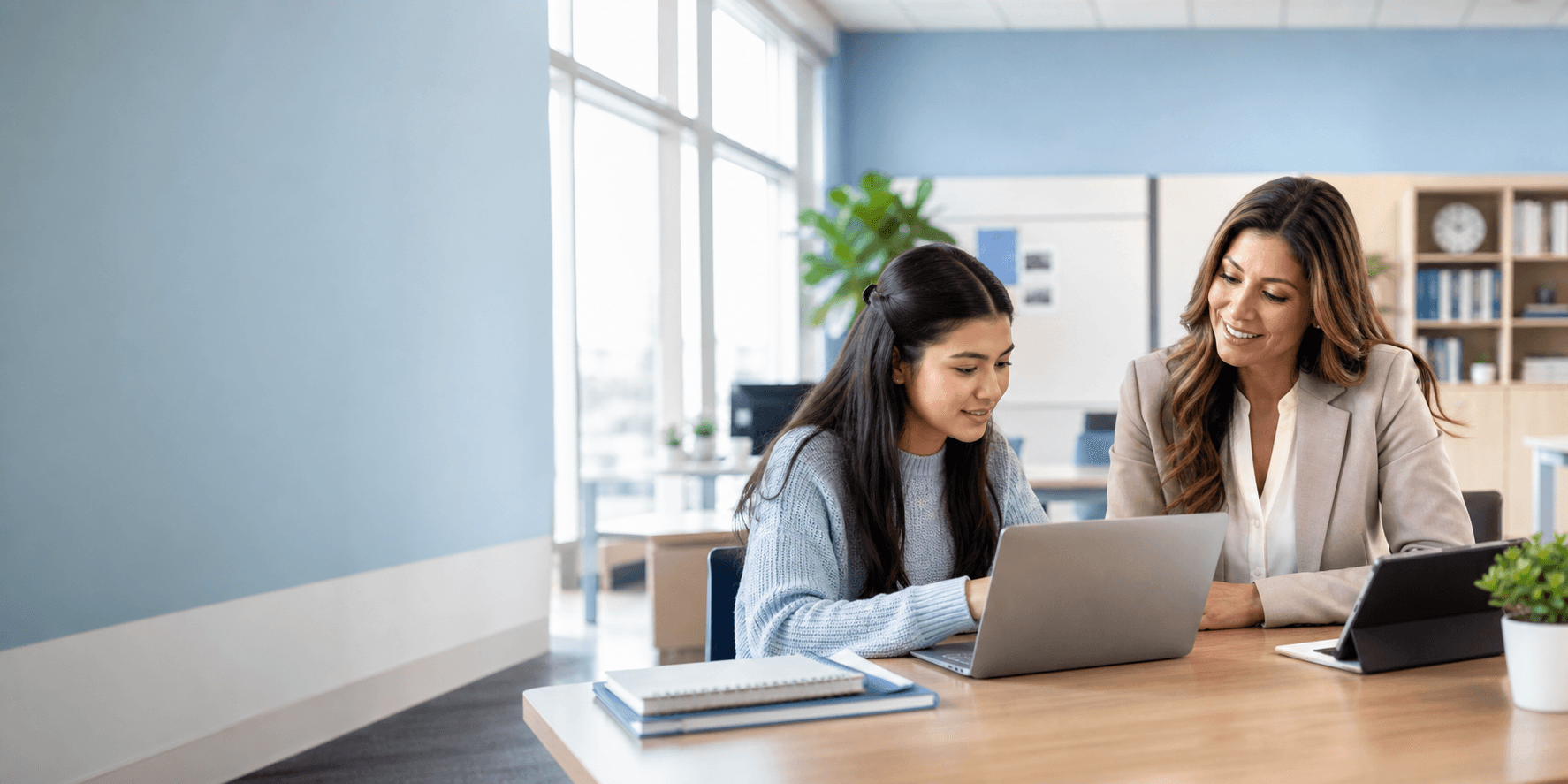 A student reviews registration details on a laptop while an education administrator helps nearby in a bright school office.